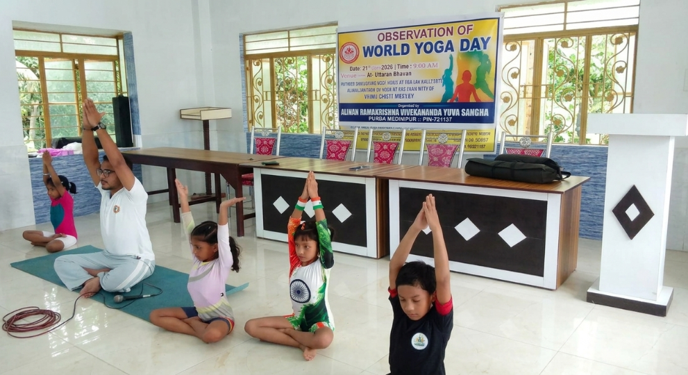 An instructor and young children sitting cross-legged on floor mats with raised overhead palms, demonstrating yoga poses during a World Yoga Day event.