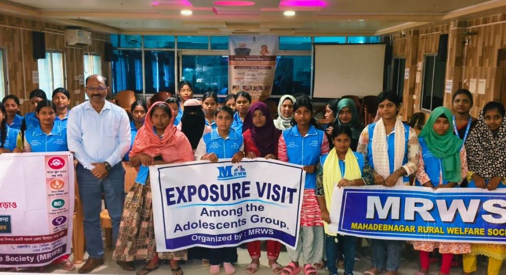 A group of young girls and organizers holding banners for an adolescent exposure visit inside a conference hall.
